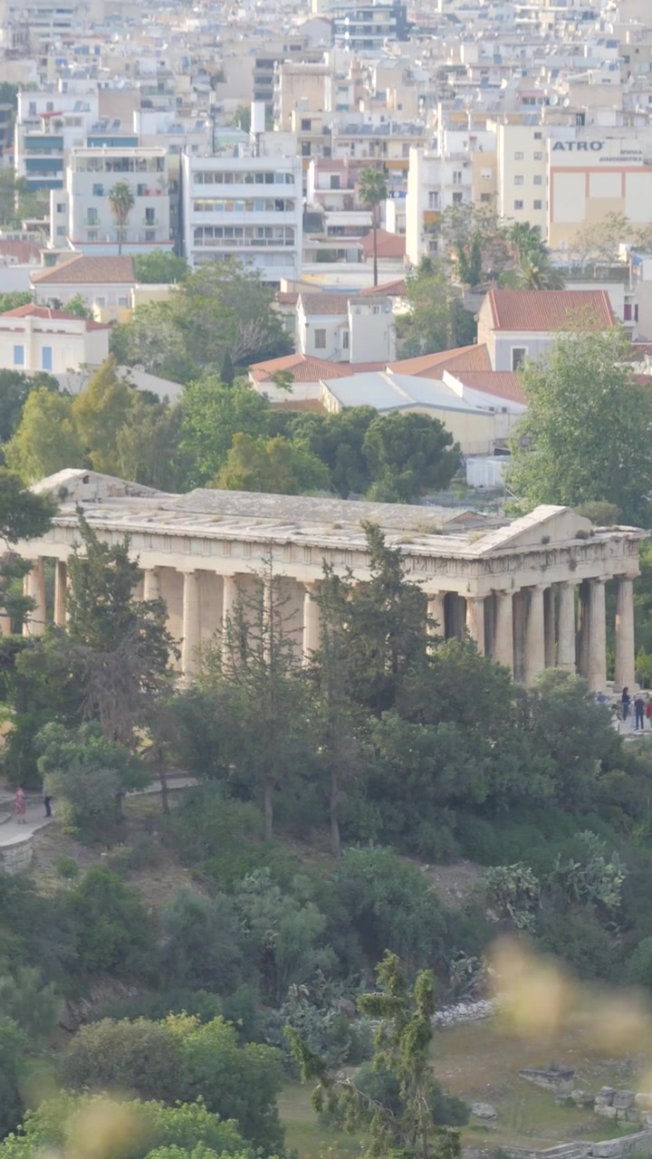 Yunanistan'da, arka planda Atina şehir manzarasıyla ağaçlarla çevrili Dorik Hephaistos Tapınağı'nın dikey görünümü.