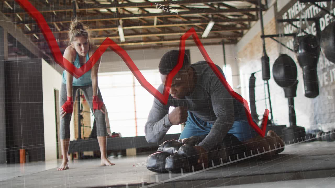 Boxing coach kneeling adjusting pad showing punches training boxer while red graph rising and fall