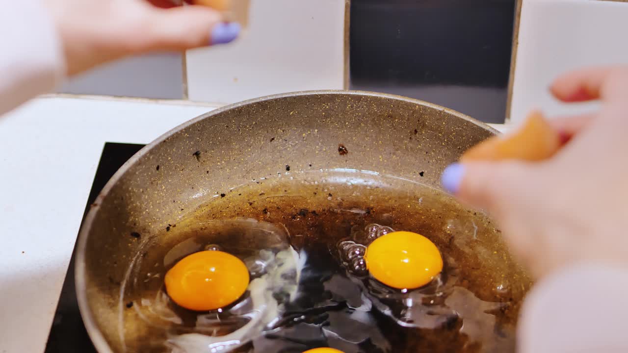Close up view of female hands cracking eggs in pan with warm kitchen light