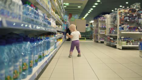 cute little child walking in water department in the supermarket and choosing bottles inside of a big marketplace, carefully