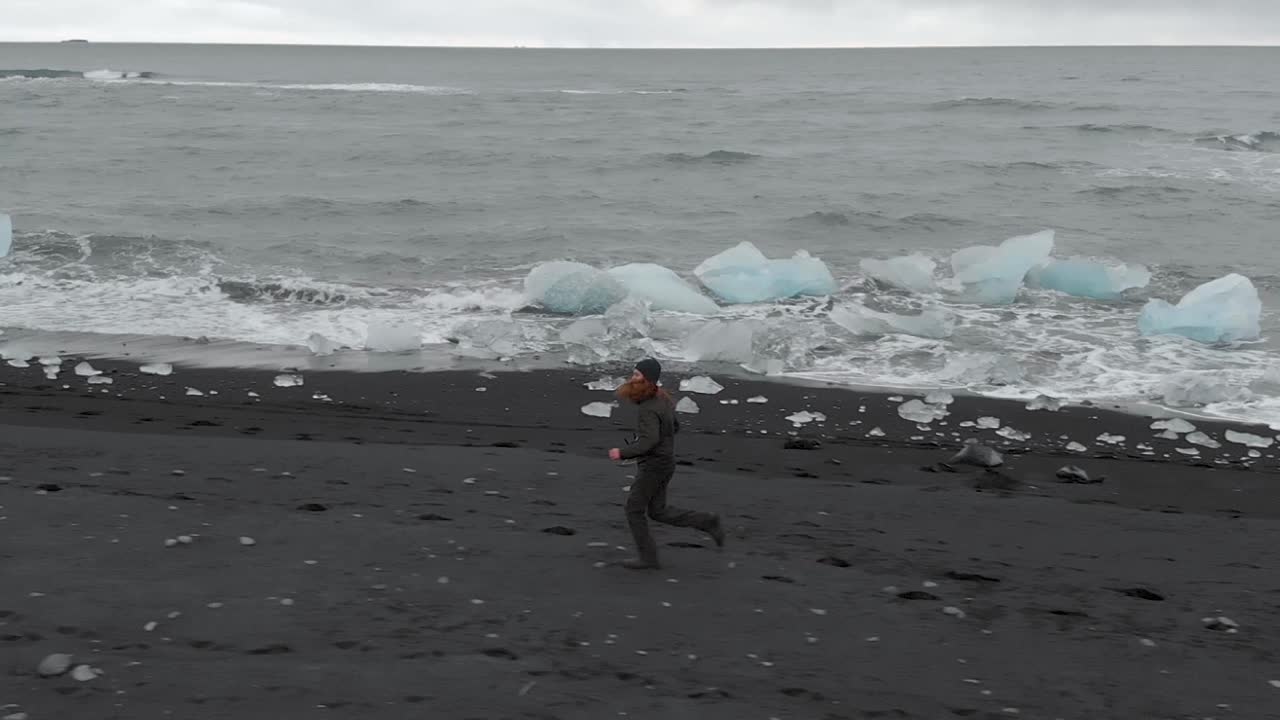검은 모래 해변을 따라 달리는 남자의 슬로우 모션 공중 샷