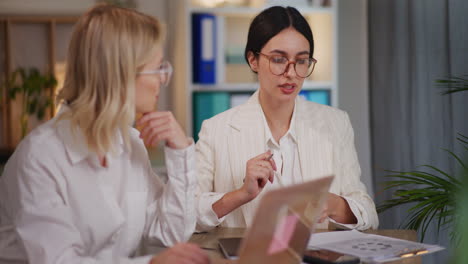 two women analyzing financial reports in office until evening