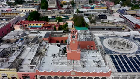 Aerial-camera-backing-away-and-pitching-up-creating-a-parallax-of-the-clock-tower-over-the-Municipal-Building-in-Merida,-Yucatan,-Mexico