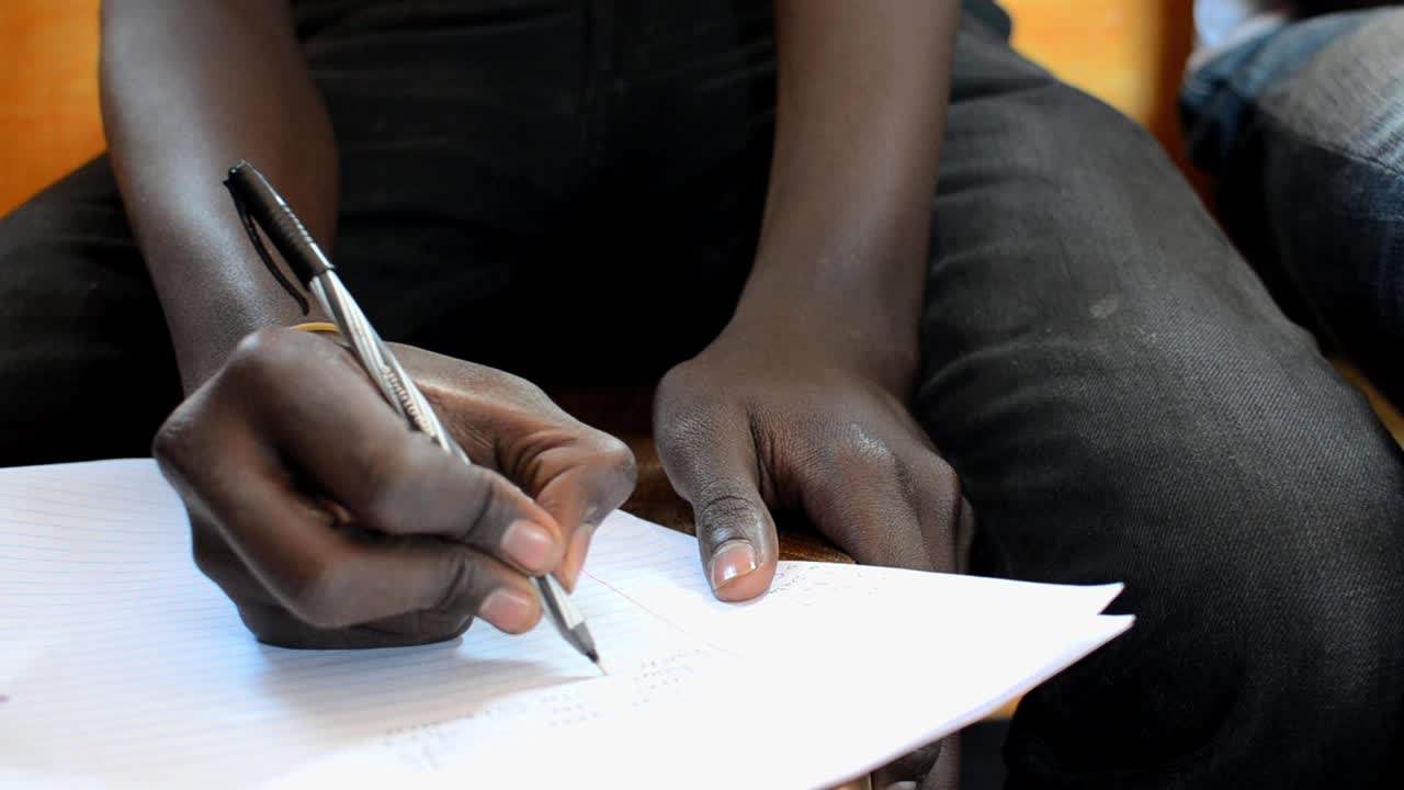 Gros plan sur la main d'un jeune homme qui écrit lors d'un séminaire à Kibera, Nairobi, Kenya 2