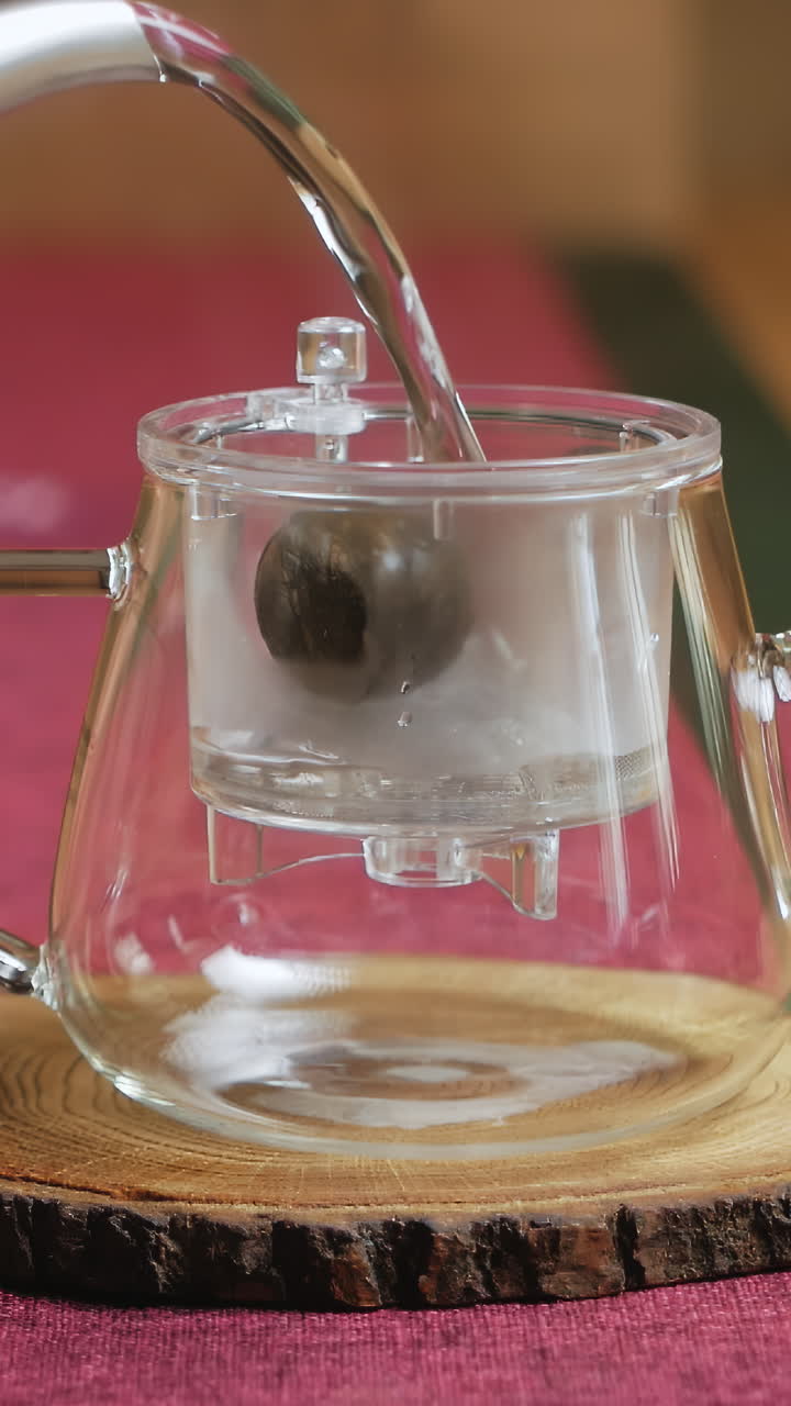 Pouring Hot Water Over Loose Leaf Tea in a Glass Teapot