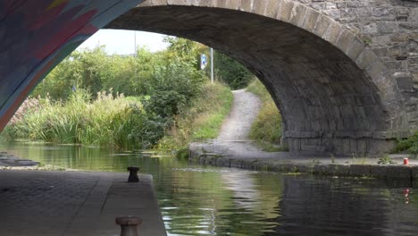 small old bridge over calm narrow river with dirt path in the background at dublin canal in ireland