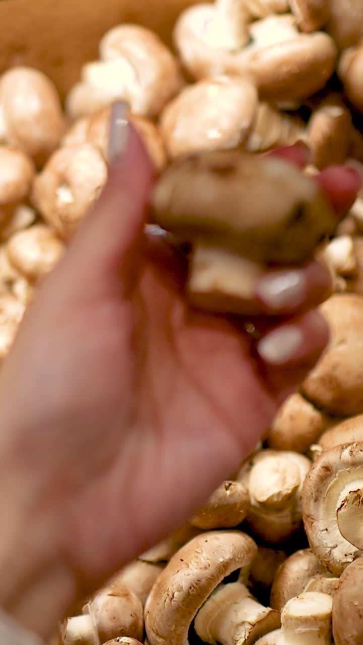 Una mano seleziona ed esamina funghi cremini sotto un'illuminazione calda in un supermercato della Gold Coast