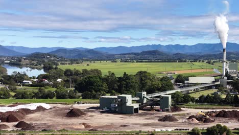 aerial footage of a sugar mill surrounded by lush fields and distant mountains under a clear sky