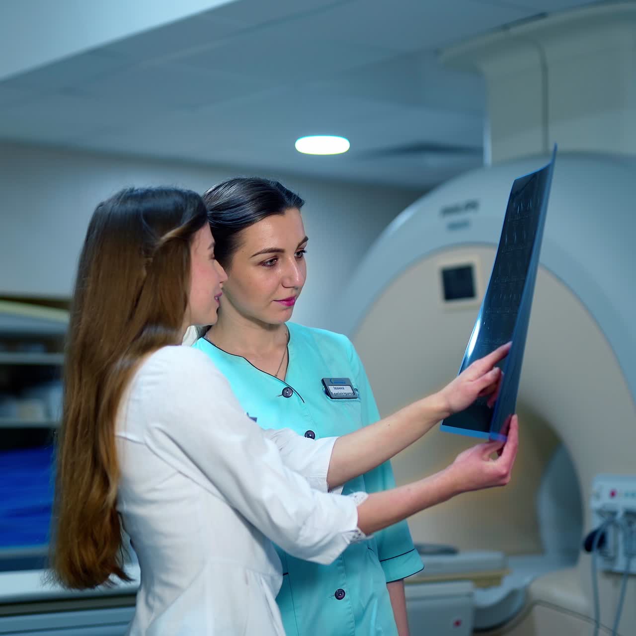 Female doctor and a nurse looking at x-ray photo. Two experts analyzing radiograph picture on the modern medical equipment background in clinic.