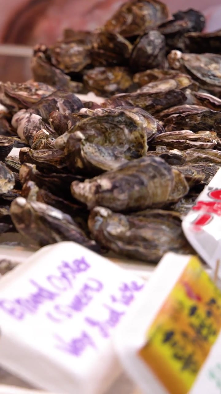 Close-up shot of raw oysters on ice at a Tokyo market with vendor hands visible.