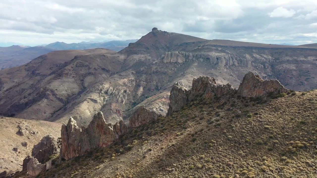 Spettacolare ampia ripresa con drone su creste rocciose uniche e affilate e pendii di valli aride nella campagna di Bariloche. Mostra il vasto paesaggio montano vulcanico, simile a un deserto, sotto un cielo estivo nuvoloso.