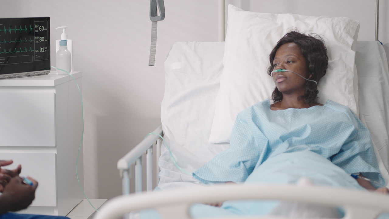 un médico africano entrevista a un paciente acostado en una cama de hospital con una máscara de oxígeno. una mujer negra acostada en una cama de hospital describe los síntomas al médico