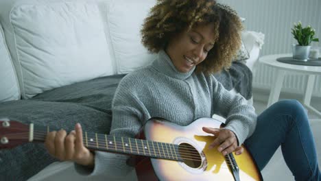 Mujer-Joven-Tocando-La-Guitarra-En-Casa