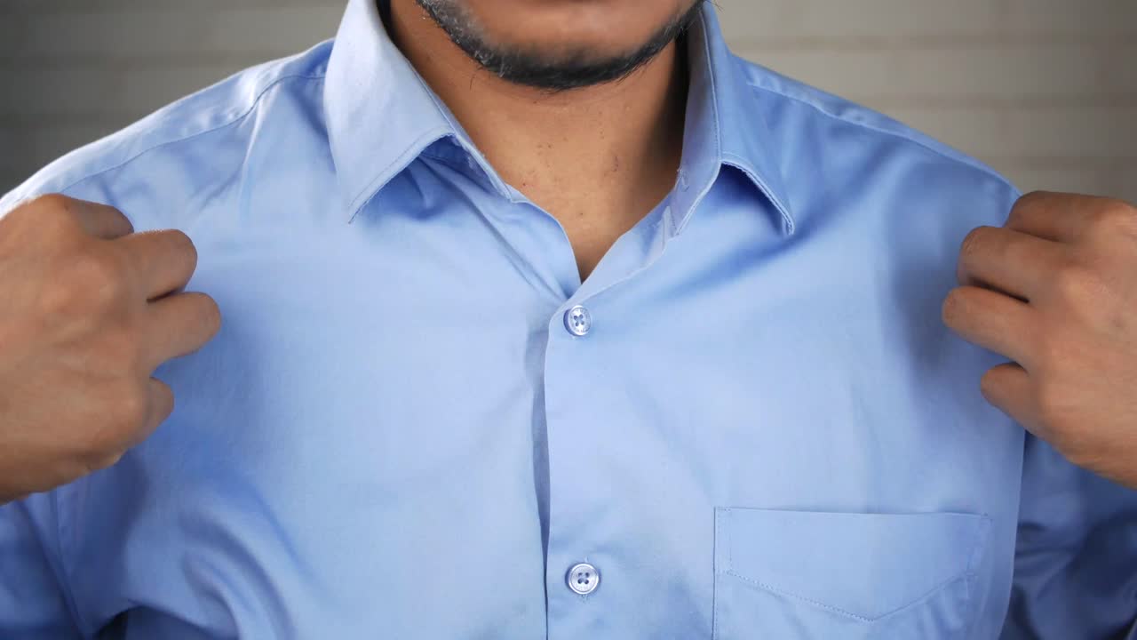 un hombre abotonando una camisa azul.
