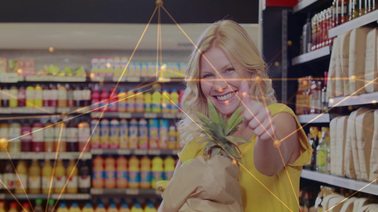 Female shopper yellow top holding brown-bag with pineapple giving thumbs-up in store under gold net