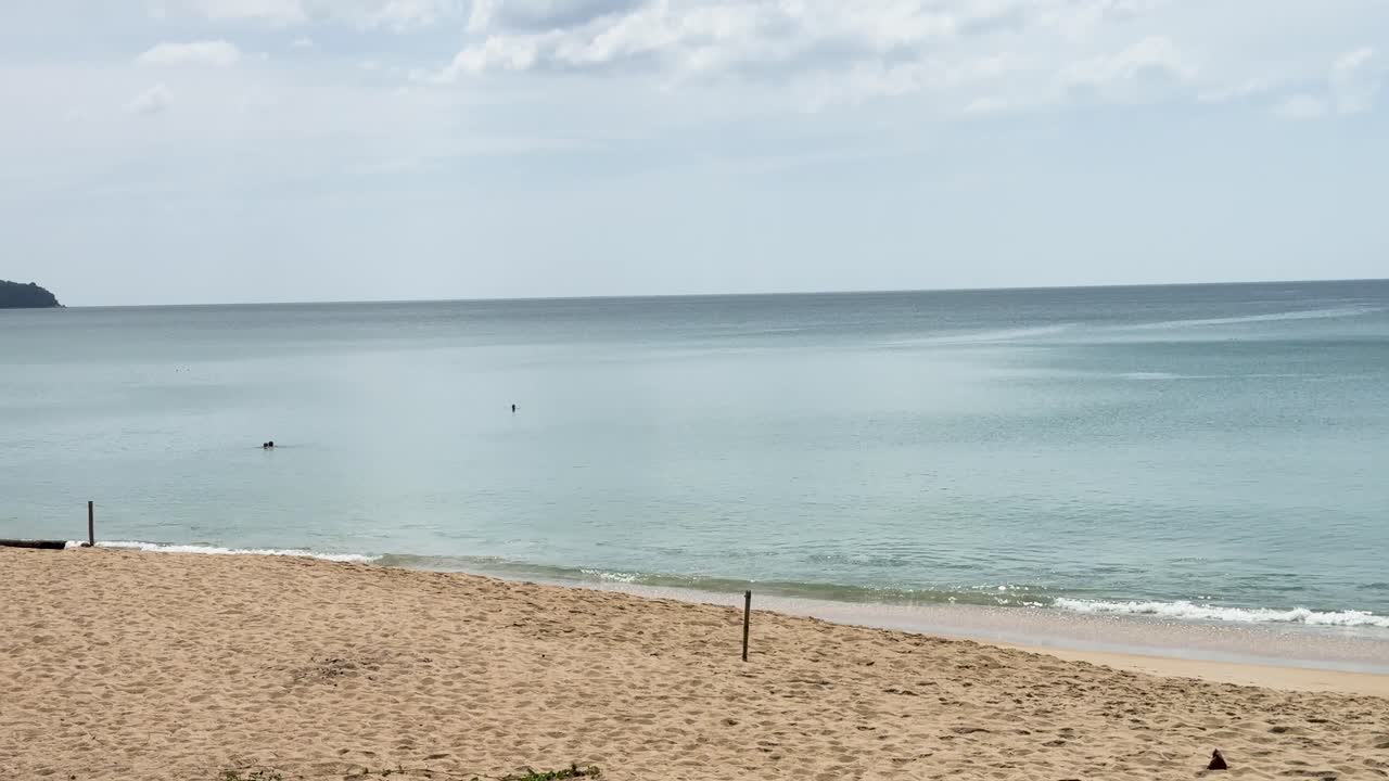 A tranquil beach scene with gentle waves and distant hills under clear skies, captured in natural daylight