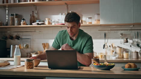pensive freelancer texting laptop at home kitchen closeup. man eating breakfast
