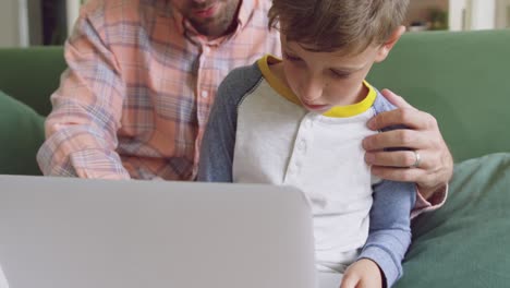 father and son using laptop on sofa at home 4k