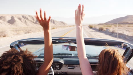 two female friends raise hands driving in an open top car