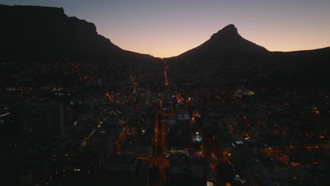 Foto-Romántica-De-La-Ciudad-Nocturna-Con-Largas-Calles-Rectas-Iluminadas-Por-Farolas-Y-Un-Colorido-Cielo-Crepuscular-Con-Siluetas-De-Montaña.-Ciudad-Del-Cabo,-Sudáfrica