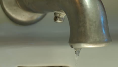 Slow-motion-medium-shot-of-a-faucet-as-the-water-runs,-shuts-off-and-drops-of-water-continue-to-drop