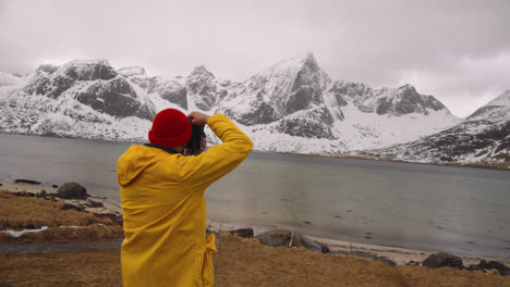 fotógrafo con chaqueta amarilla tomando instantáneas de montañas nevadas en lofoten noruega - toma panorámica