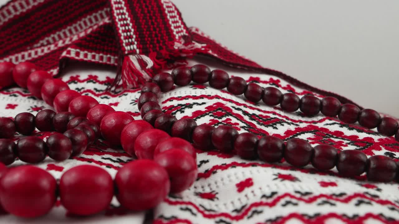 Perline rosse, cintura decorativa e rametti di viburno su tessuto ricamato