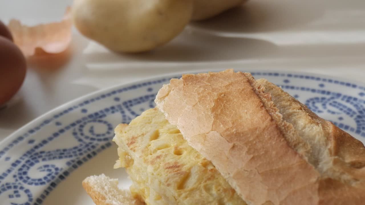 Tasty Spanish bocadillo tortilla sandwich on a plate with eggs nearby