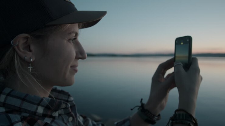 Happy Woman Photographing Sunset over Lake with Phone