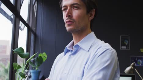 hombre de negocios caucásico de pie mirando por la ventana en una oficina moderna