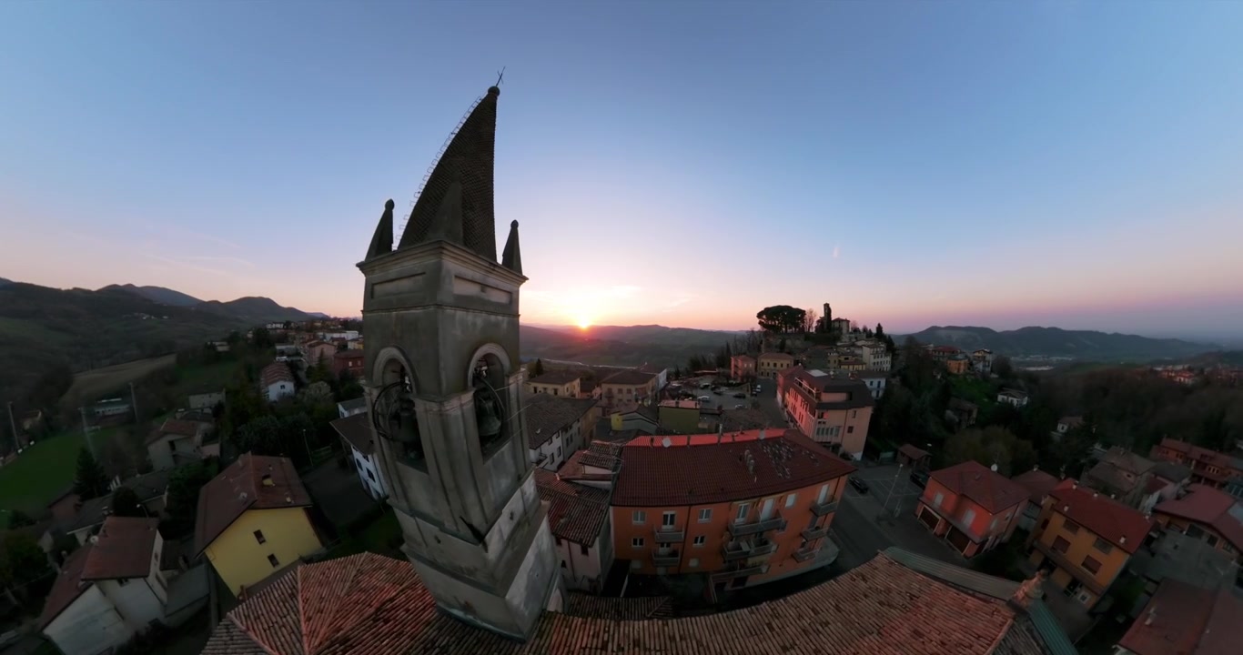 Kirkeklokketårn og landsbyhuse oplyst af den nedgående sol, Piacenza-provinsen i Italien. Luftoptagelse fremad, plads til tekst
