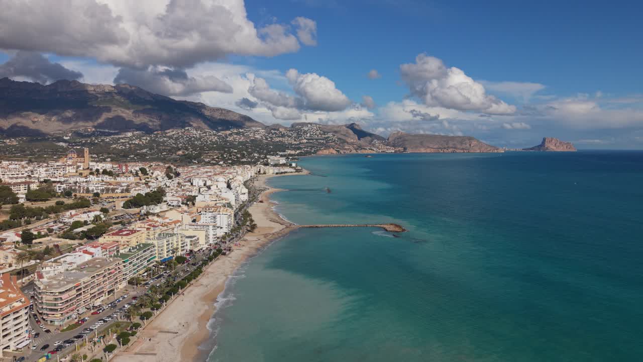 Albir e Altea, Costa Blanca, Espanha. Drone voando ao longo da praia e da orla marítima com água azul calma e cristalina e um cenário de montanhas e nuvens interessantes sob sol forte