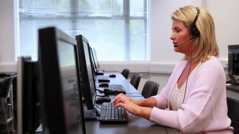 mujer escribiendo en la computadora mientras habla con auriculares.