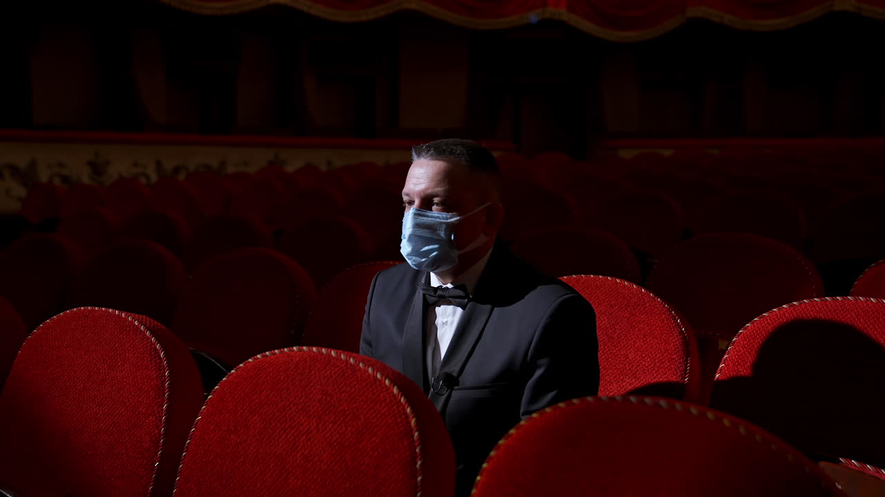 Man sits in the middle of empty theater hall with red velvet chairs. Actor is alone in theater. Lockdown and pandemic concept.
