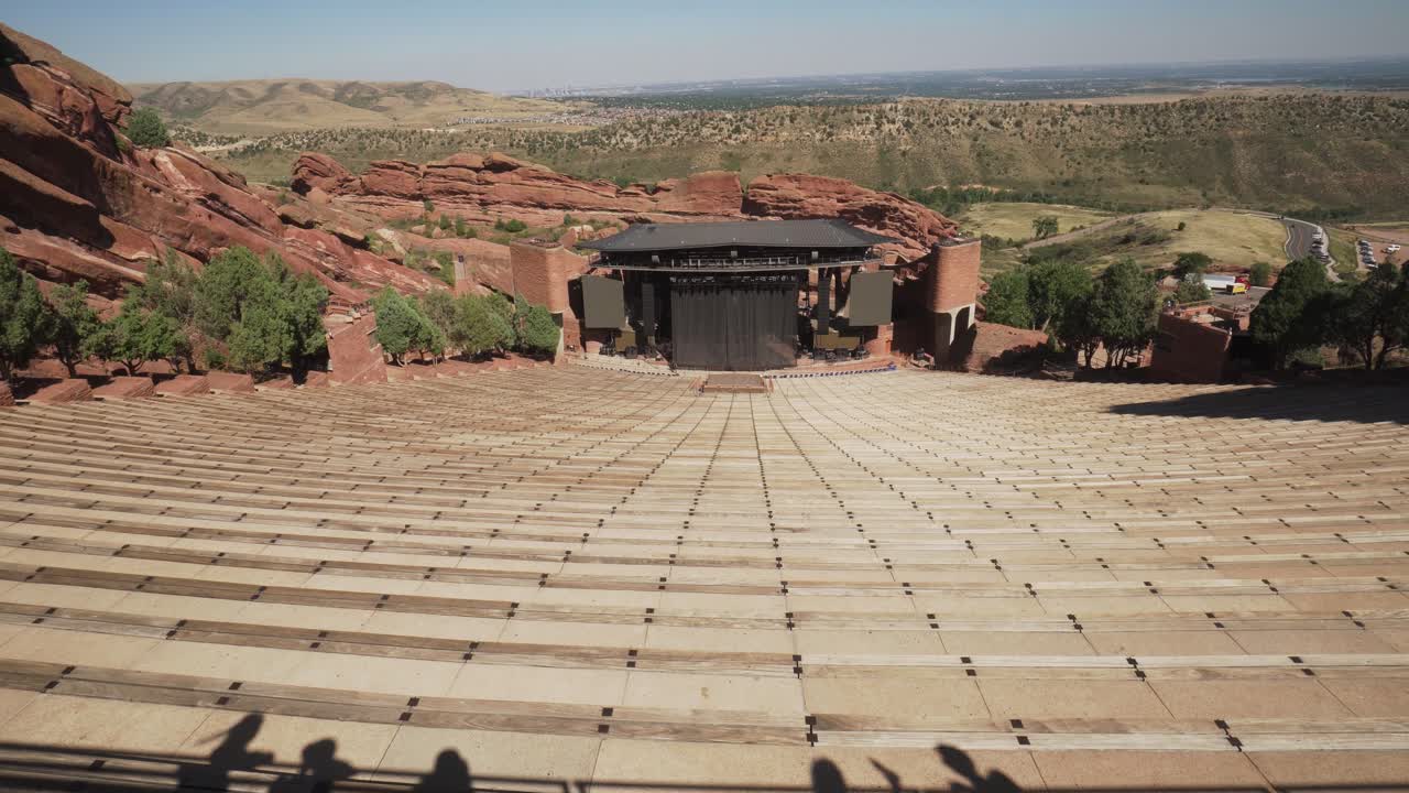 Red Rocks Amphitheater being prepared for a concert, overlooking Denver, daytime. Pan Up From Seats