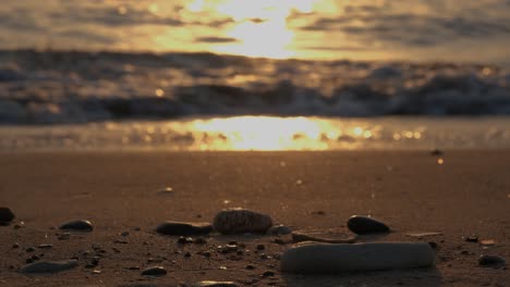 relajante vista a la playa de guijarros en la arena con olas en el fondo bajo una puesta de sol dorada