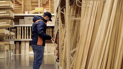 young guy chooses wooden beams in building materials store