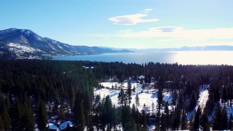 aerial drone shot, flying over the woods towards the crystal clear water with the sun's reflection in lake tahoe, nevada-california