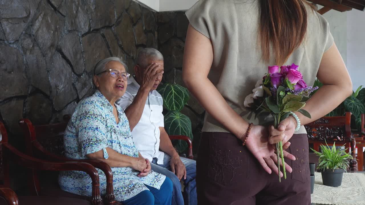 Giovane donna asiatica sorprende i genitori con fiori e li abbraccia