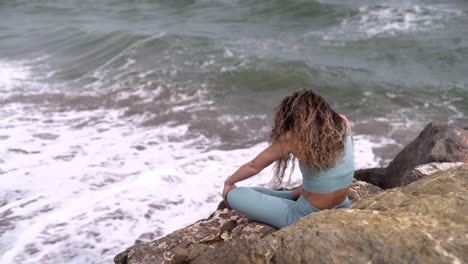 mujer caucásica con rizos estirando su cuerpo junto al océano