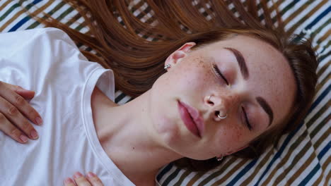 close-up of a young woman with freckles and a nose ring sleeping peacefully on a striped bed