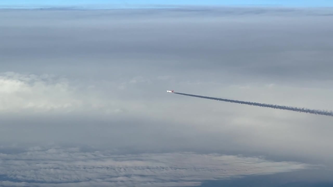 Højre side cockpitudsigt af et jetfly, der flyver over skylag og efterlader en sort kondensstribe.