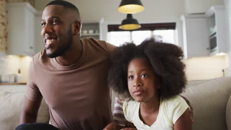 african american daughter and her father on couch watching tv eating popcorn and cheering