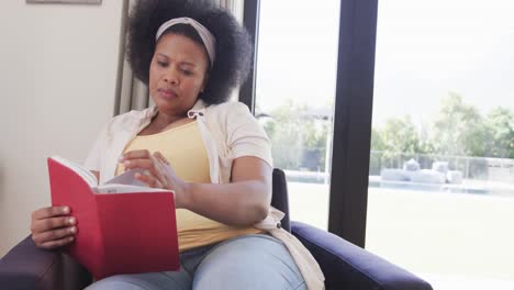 African-american-plus-size-woman-sitting-in-armchair-and-reading-book,-unaltered,-slow-motion