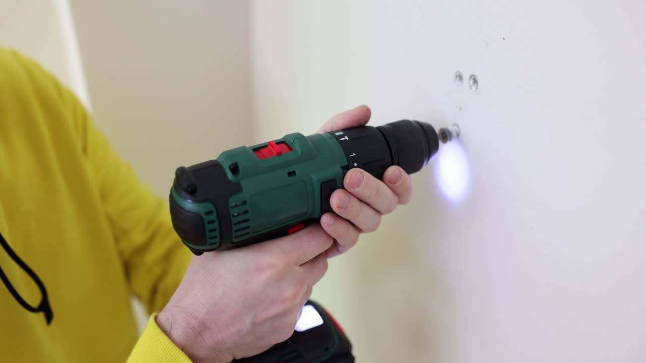 Worker unscrews fixture with electric screwdriver in premise