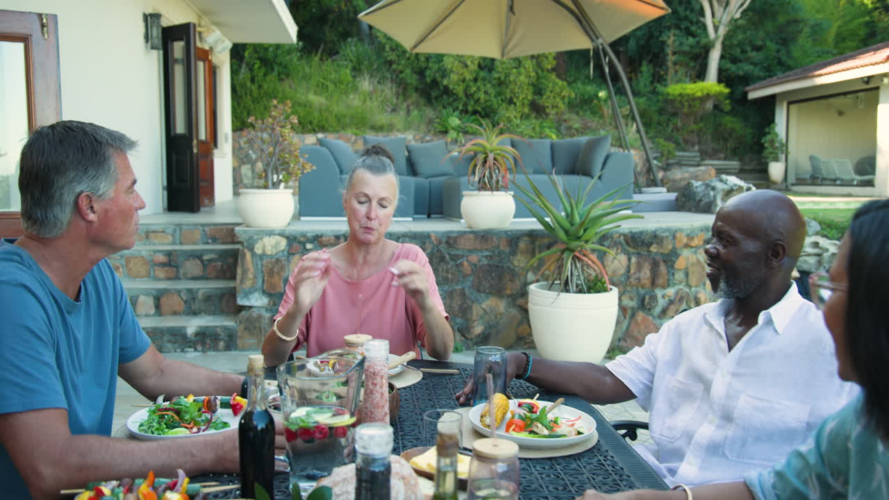 Diverse senior friends enjoying in garden dinner together, sharing laughter and delicious food