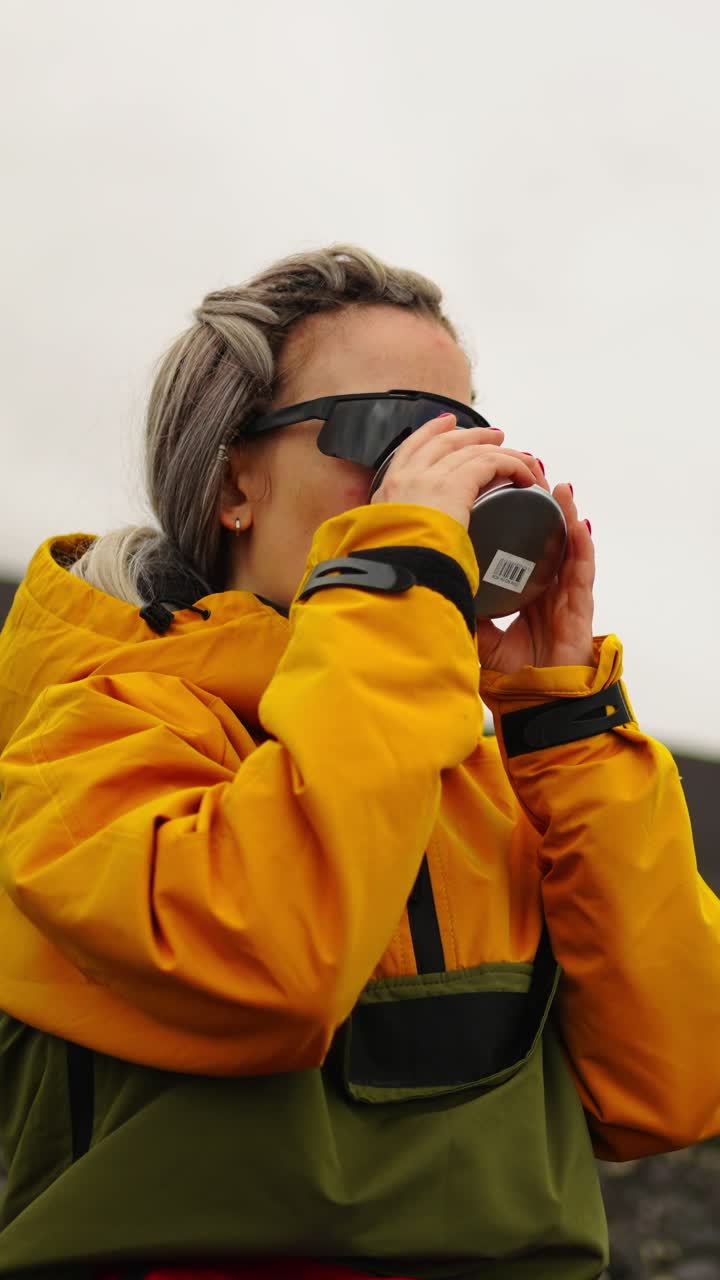 Donna con giacca gialla che beve una bevanda calda all'aperto