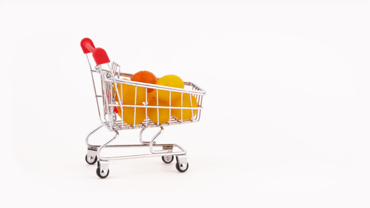 Sich bewegender Einkaufswagen gefüllt mit einem Stapel gelber Kirschtomaten mit Wassertropfen. Isoliert auf weißem Hintergrund. Nahaufnahme. Makro