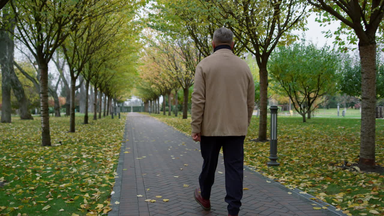 Casual man walking through park covered in autumn leaves