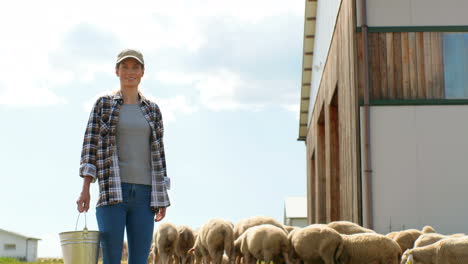 Portrait-of-Caucasian-young-woman-farmer-in-hat-standing-outdoor-at-shed-and-holding-bucket-with-food-or-water-for-cattle